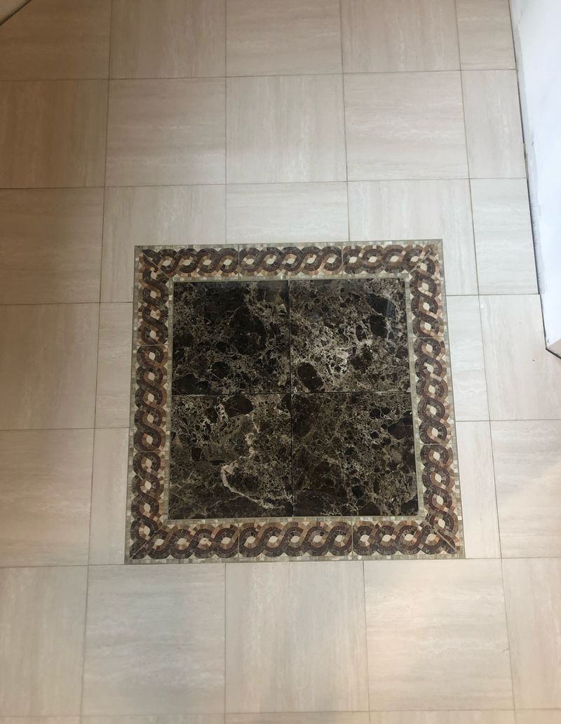 Dark stone floor inset framed by a braided mosaic border within pale field tile