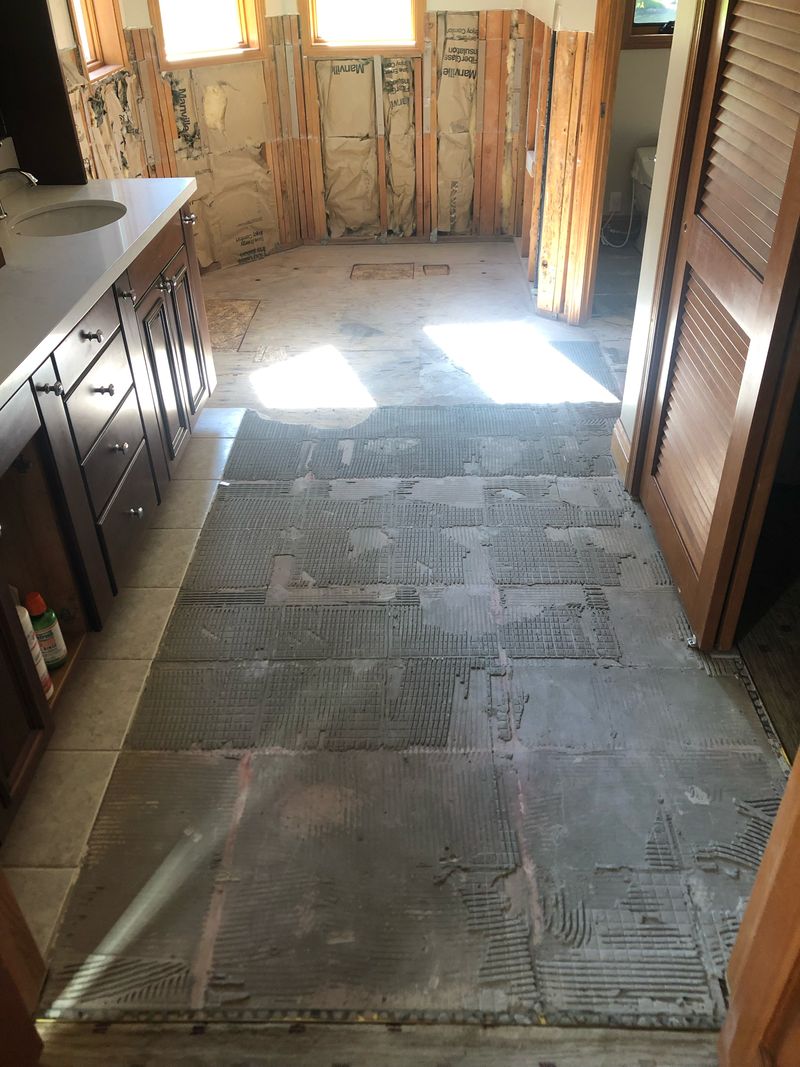 Bathroom floor stripped of its old tile down to the thinset, with the far wall opened to the studs and insulation