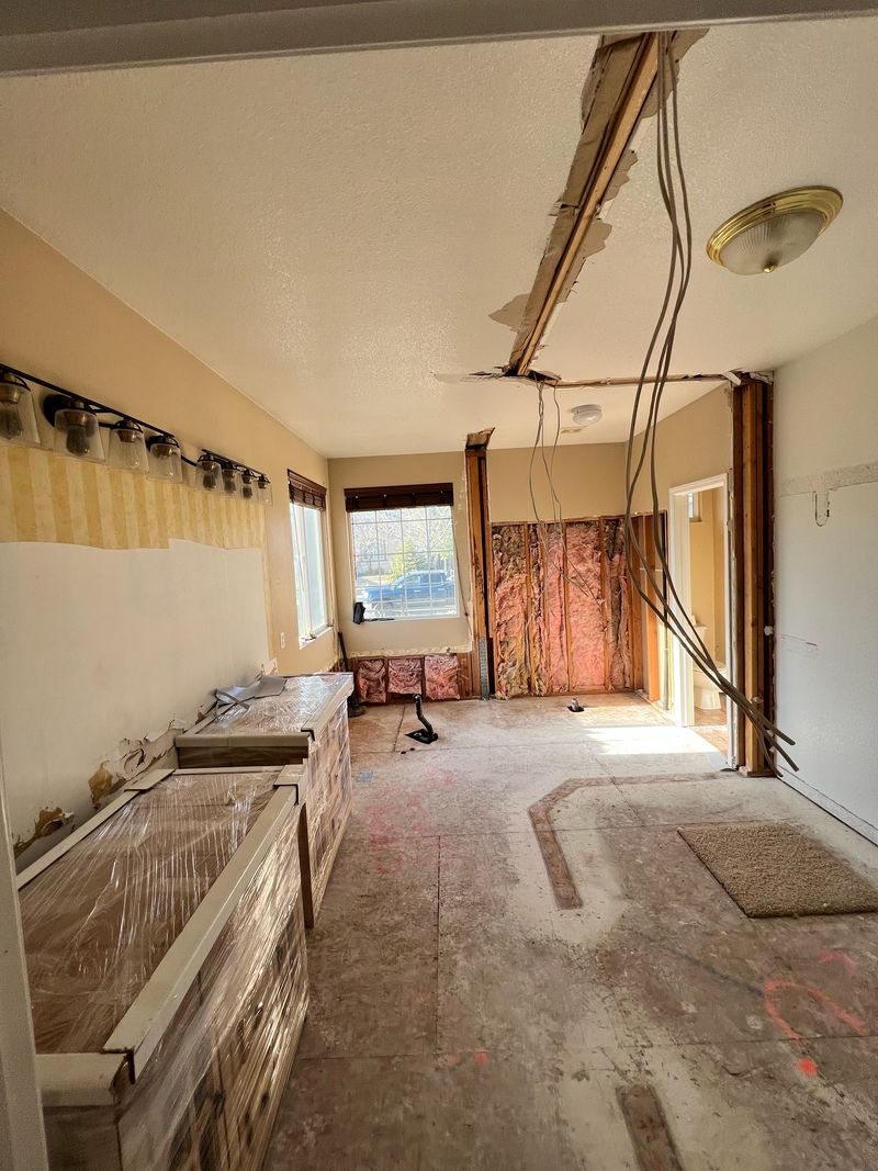 Bathroom opened up for a remodel: ceiling and walls cut back to the framing, wiring pulled down, subfloor bare