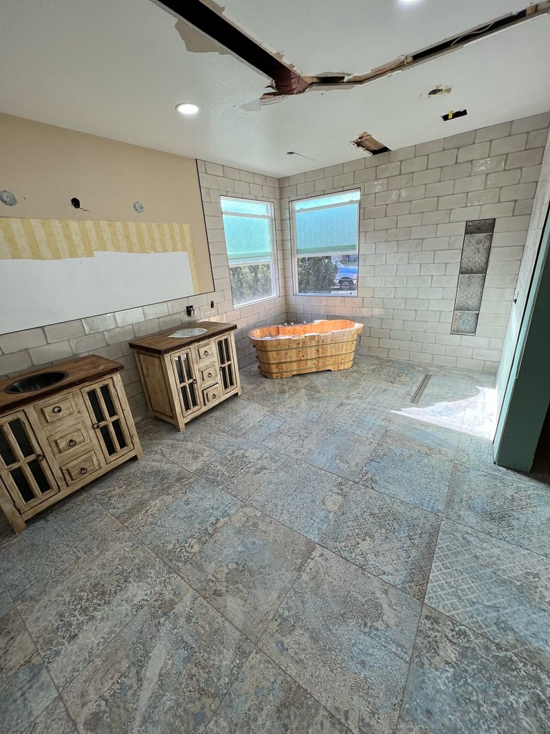 Patterned floor tile and white wall tile set, with a wooden soaking tub and two vanities placed and the ceiling still open