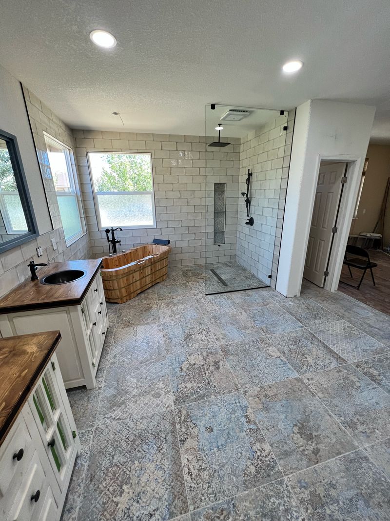 Bathroom near completion with a walk-in shower behind a glass panel, a wooden soaking tub and two wood-topped vanities