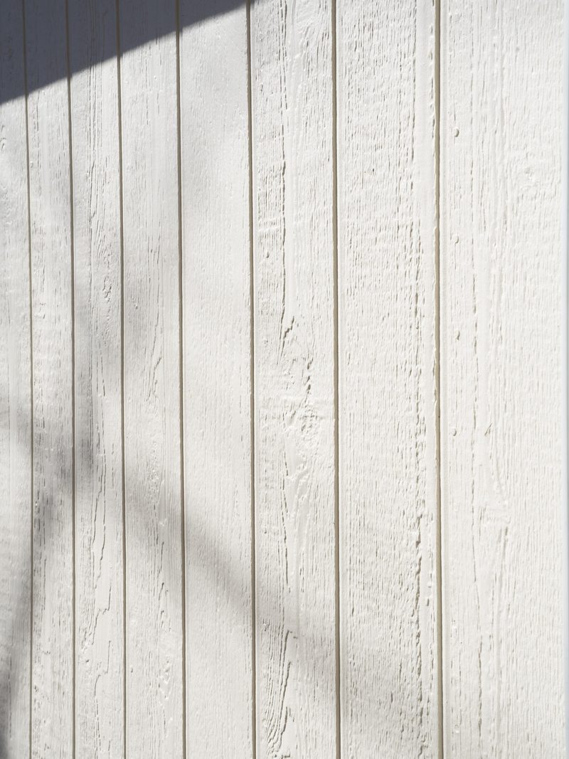 Close view of painted vertical board-and-batten siding with the shadow of a branch across it