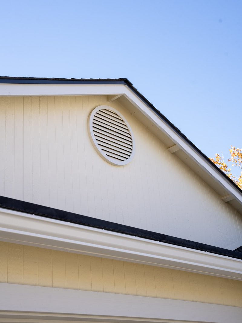 Gable end and eave of a house: the fascia line, the return at the eave and a round louvred vent under the ridge