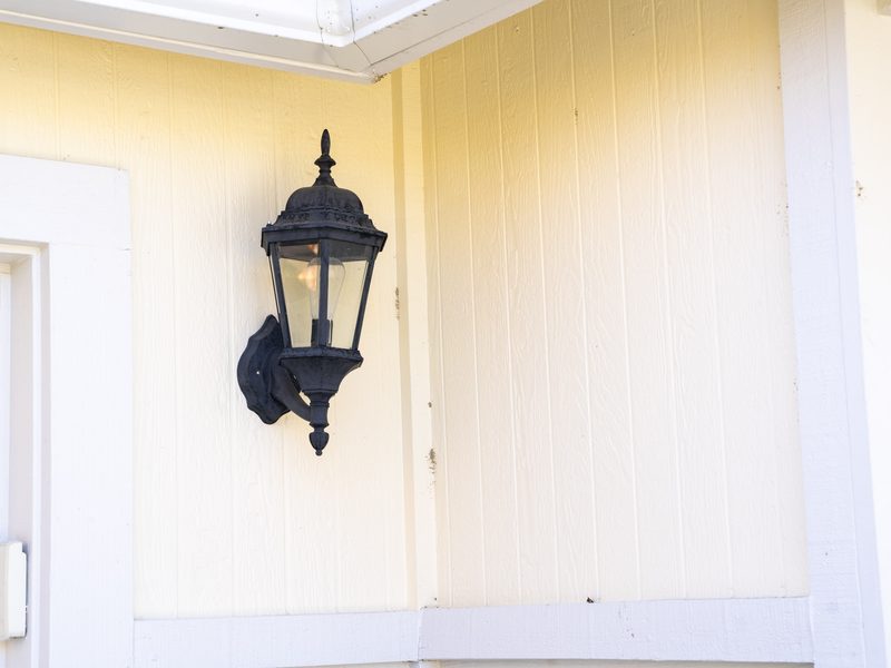 A black carriage-style lantern mounted on painted vertical siding beside a white door casing