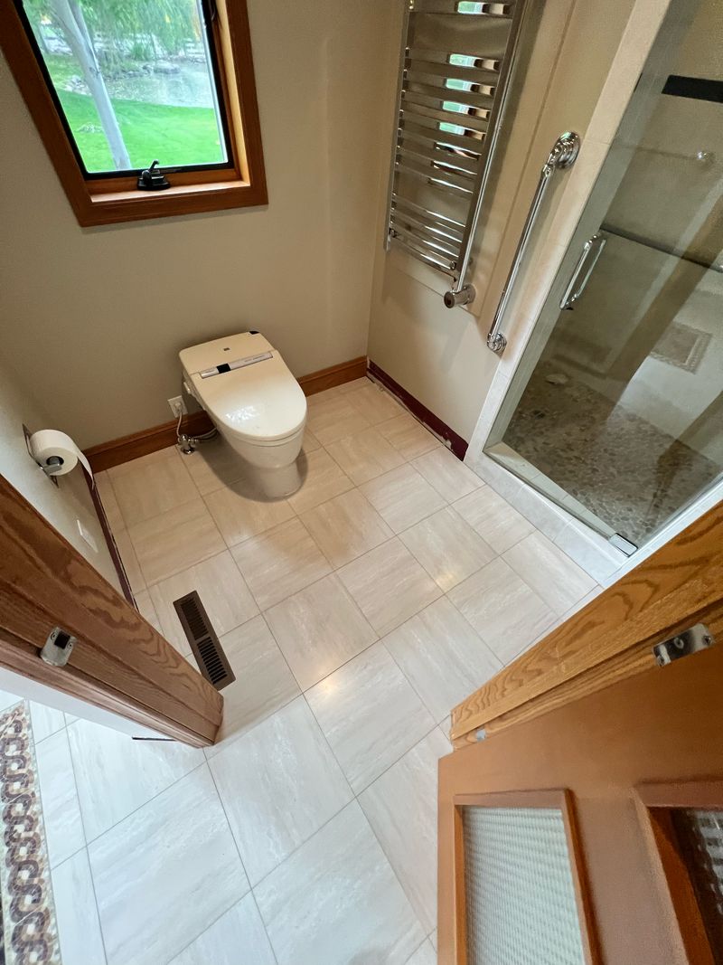 Finished bathroom with a pale tile floor, a toilet, a wall-mounted towel warmer and a glass shower