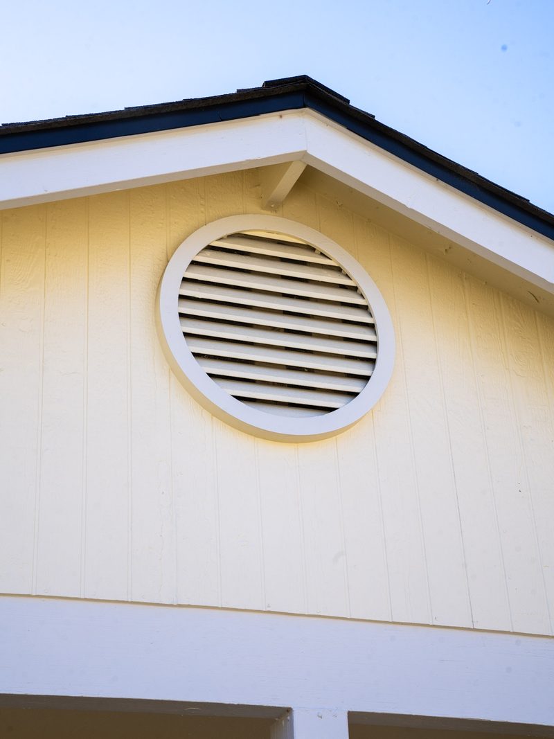 Gable end of a re-sided house: a round louvred vent set into new vertical siding under a dark fascia return