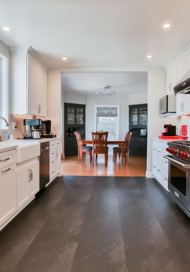 Galley kitchen with white shaker cabinets and a dark tile floor, opening through a wide doorway to the dining room