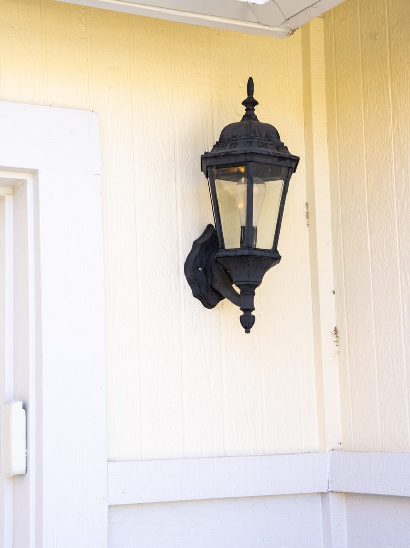 A black carriage lantern remounted on new painted siding beside a white door casing