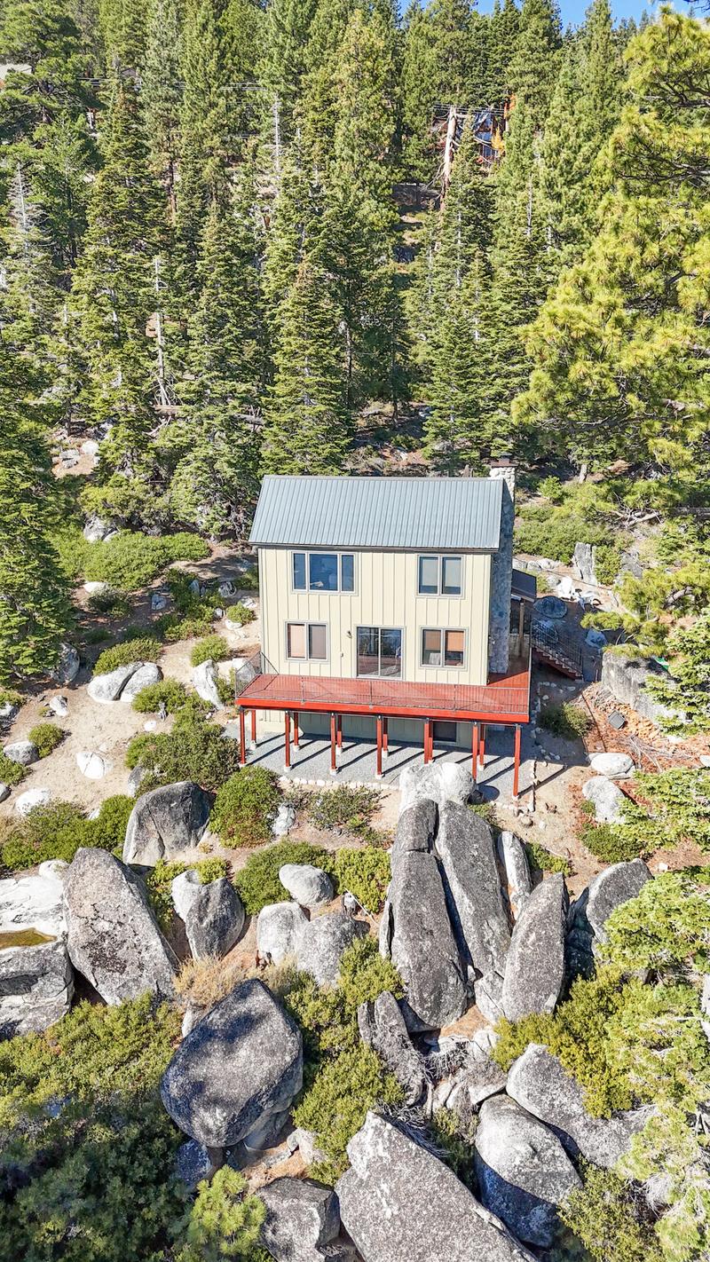 Aerial view of a two-storey house with a red-framed deck built among granite boulders and pines above Lake Tahoe