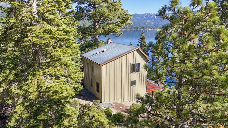 Aerial view of a green-sided house among tall pines with Lake Tahoe and the far shore beyond